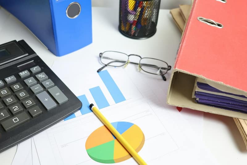 A desk with a calculator, glasses, ring binders and printed charts