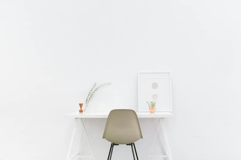 A minimal white desk with a small plant and a pale chair against a white wall